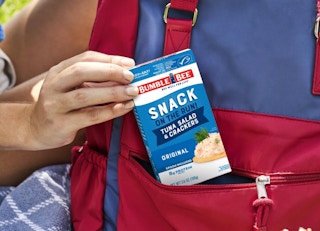 a hand putting a tuna kit in a red backpack