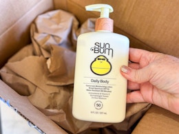 holding Sum Bum lotion over opened Amazon prime box