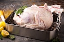 An uncooked turkey in a pan with other ingredients around it