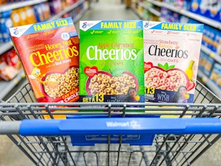 A green, red, and pink box of Cheerios cereal in a Walmart cart
