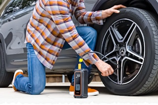 Lifestyle image of person using the Ophanie Tire Inflator Tool to inflate a car tire.