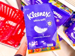 hand holding a kleenex tissues 6-pack in front of a target cart