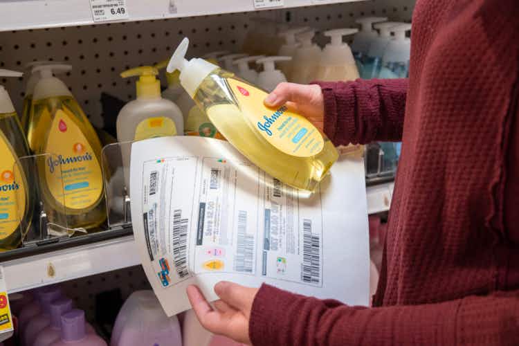  person holding paper with coupons on it while holding a bottle of baby shampoo in front of store shelves with baby shampoo on them.