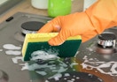a hand cleaning a stove with a sponge