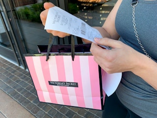 Woman looking at a receipt with shopping bag in hand.