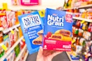 person holding 2 boxes of kelloggs nutri-grain bars in an aisle