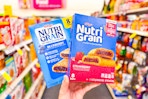 person holding 2 boxes of kelloggs nutri-grain bars in an aisle