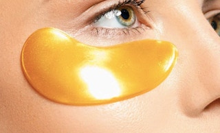 close up of a persons eye with a gold under eye hydrating mask patch