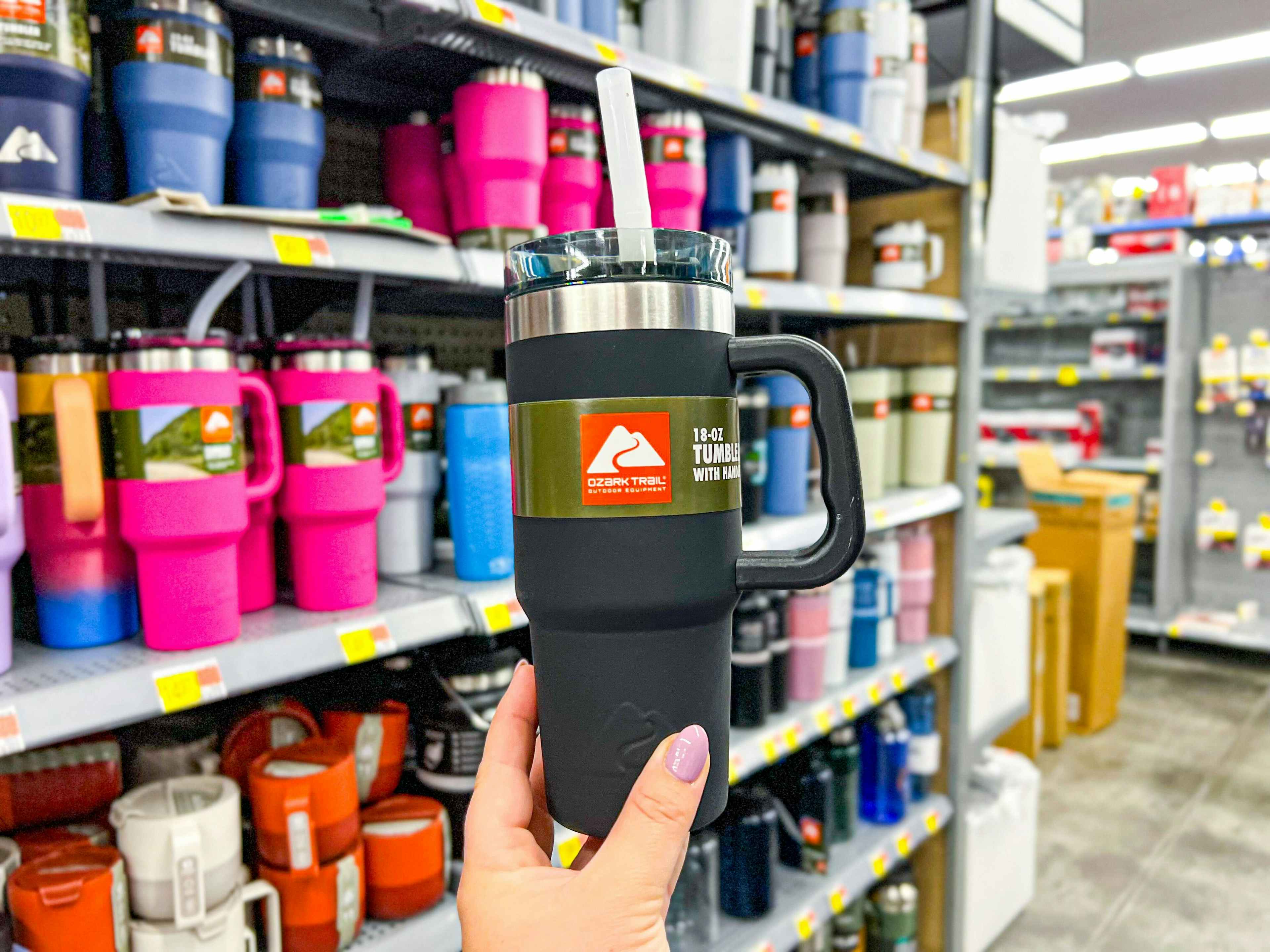 person holding a black ozark trail tumbler in front of a display