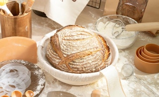 sourdough bread in a bowl on a table with baking tools and flour