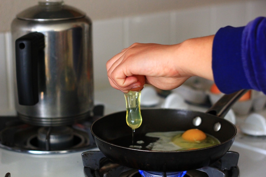 cracking eggs above a frying pan