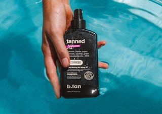 a hand holding a bottle of tanning oil above water