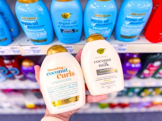 hand holding out two bottles of ogx shampoo in front of a shampoo aisle at cvs