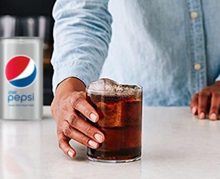 Someone holding a glass of Diet Pepsi on the table