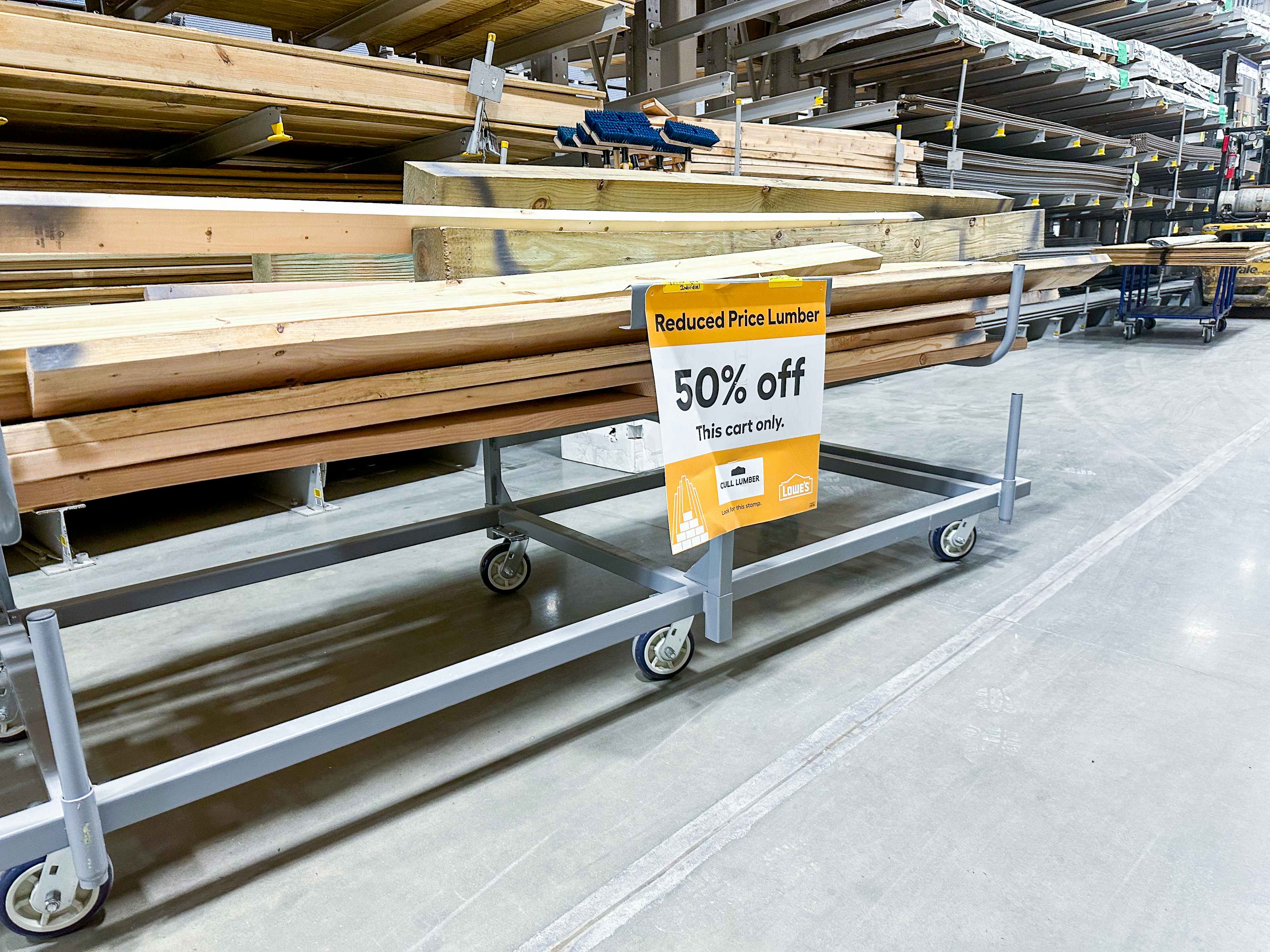 A cart stacked with scrap wood in the Lowe's lumber department with a 50% off sign