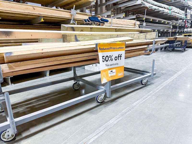 A cart stacked with scrap wood in the Lowe's lumber department with a 50% off sign