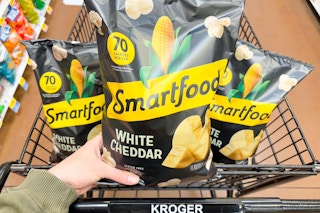 hand holding a bag of smartfood popcorn on kroger shopping cart