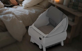a self-cleaning litter box next to a bed