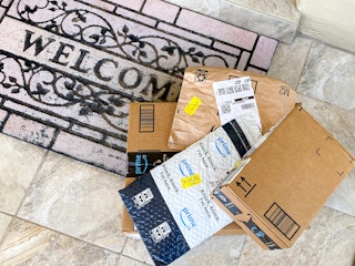 A pile of Amazon boxes and Amazon packing envelopes sitting on a doormat outside a front door.