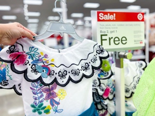 Encanto Dress Costume held up in front of sale sign for Buy 2, get 1 free in stores at Target