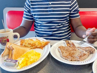 A person sitting in a booth at Waffle House with plates of food and a coffee mug sitting on the table in front of them.