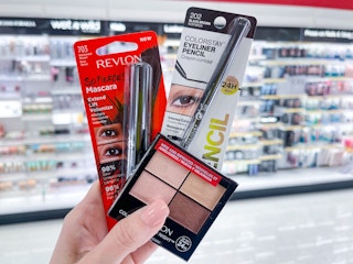 A variety of Revlon make up held out by hand in front of a store aisle.