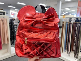 A red Disney bag held out by hand in front of a store aisle.