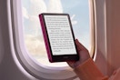 A hand holds the Kindle Paperwhite near an airplane window. The sun doesn't wash out the screen.