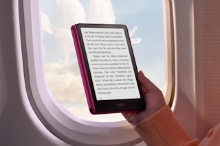 A hand holds the Kindle Paperwhite near an airplane window. The sun doesn't wash out the screen.