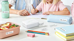a label maker on a table with stationery, books, and a lunch bento box