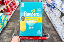 person pushing a cart with pampers swaddlers diapers in it