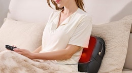 a person sitting on a bed with an electric back massager