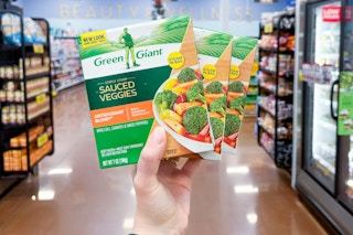 hand holding boxes of green giant vegetables