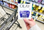 person holding an olay moisturizer over a walgreens cart