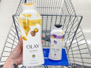 a hand holding a bottle of body wash over a shopping cart