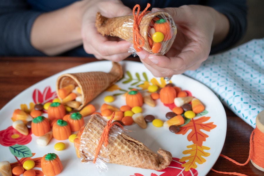 A person filling ice cream cones with candy.