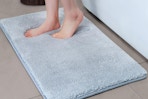 Two feet step on a plush bath mat that is light blue-grey