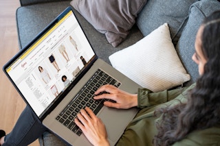 A woman sitting on a sofa with a laptop computer on her lap, looking womens apparel on at 6pm.com.
