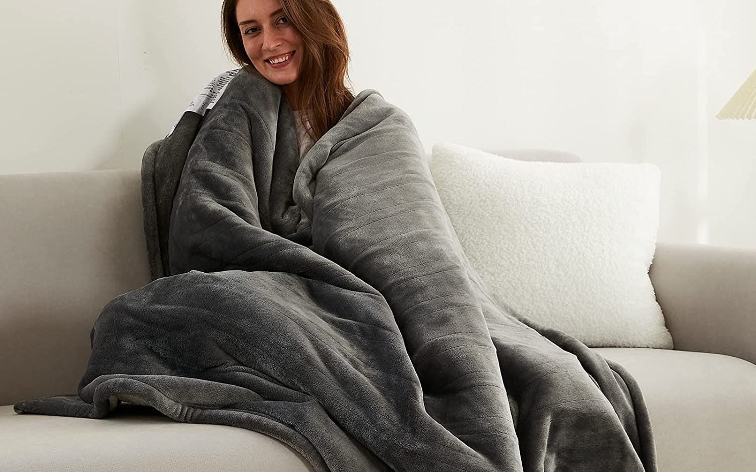 A woman wearing a blanket while sitting on a couch.