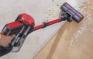 a hand using a cordless stick vacuum to clean up a spill