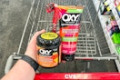 hand holding two Oxy skincare products in front of CVS cart