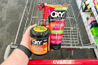 hand holding two Oxy skincare products in front of CVS cart