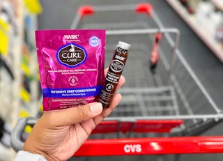 hand holding one Hask hair treatment mask with hair oil vial in front of shopping cart