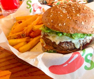A close-up of a Chili's burger in a basket with fries.