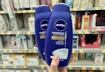 A hand holding Nivea body wash in a store aisle.