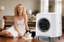 Self-Cleaning Cat Litter Box B0F6717829 A woman sits on a hardwood floor next to a black and white cat and self cleaning litter box.
