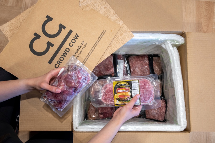 A person taking packaged meat out of a Crowd cow meat delivery box.