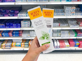 hand holding two boxes of Burt's Bees toothpaste in front of toothpaste aisle at Target