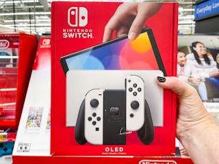 A person holding up a Nintendo Switch OLED in the Nintendo video game aisle.