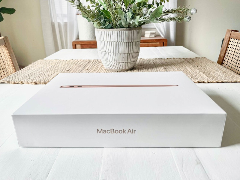 A Macbook box on a table with a plant in the background.